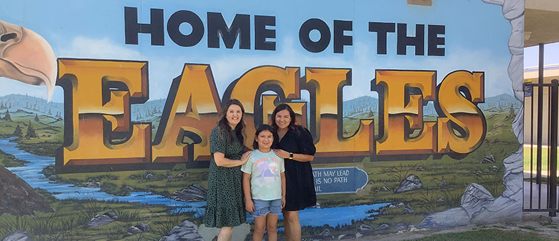 Teachers and student standing in front of the Home of the Eagles mural