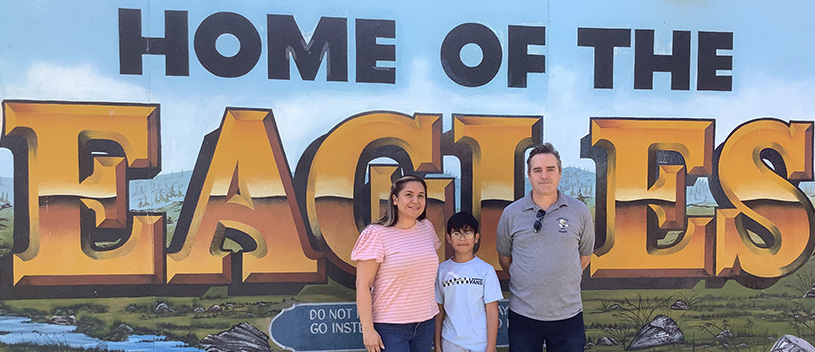 student and adults in front of Home of the Eagles sign