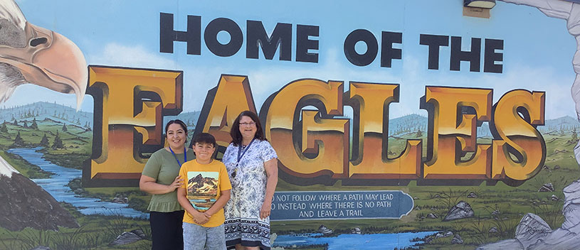 Teachers and student standing in front of the Home of the Eagles mural
